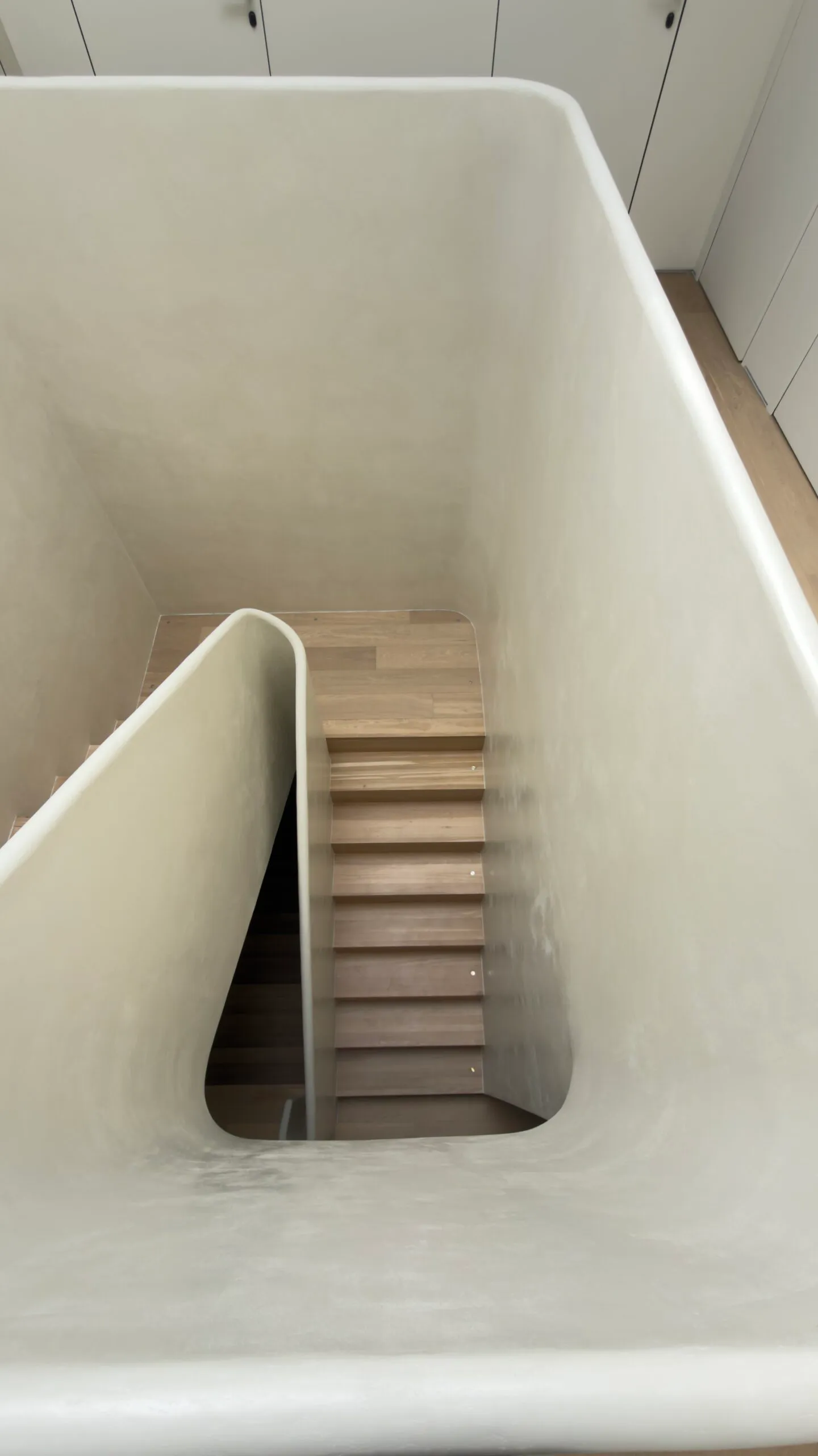 Stairwell wrapped in seamless microcement, with a rounded sculpted handrail.