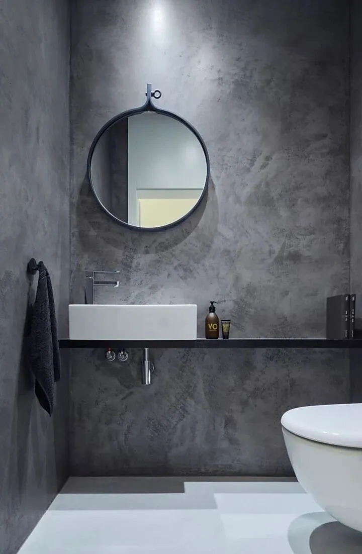 Powder room in charcoal Venetian plaster: walls with cloudy mineral depth, a black slab shelf, a round mirror and a white basin.
